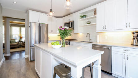 White contemporary kitchen. Stainless steel Kitchenaid appliances, white cupboards, white countertop, gray laminate floors. Soft undercabinet lighting.