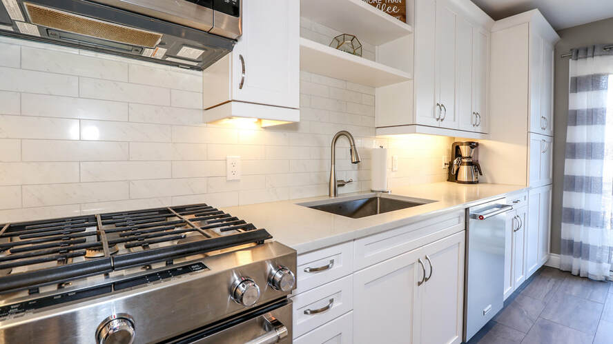 White subway tile backsplash in a modern kitchen. White cupboards, stainless steel appliances. 