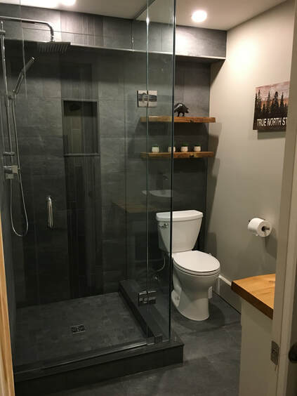 Rustic renovated bathroom - dark gray tiles, glass shower walls. 