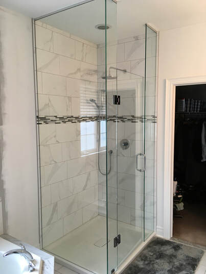 Renovated shower stall. Glass panels, white marble-style tile. 