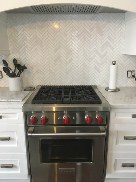Beautiful herringbone tile backsplash in a contemporary kitchen. Wolf stove and marble countertops.